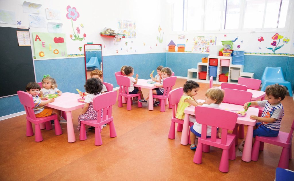 Niños y niñas pequeños sentados en sillas y mesas rosas en una clase